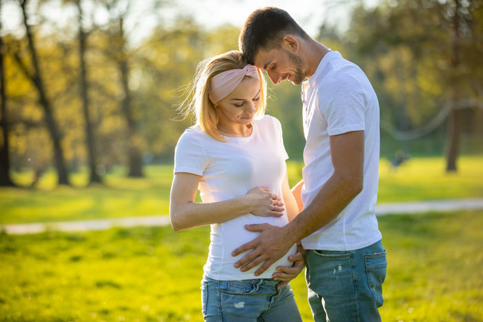 Expectant couple outdoors, man and woman bonding over pregnancy, reflecting family relationship and grandkid themes.