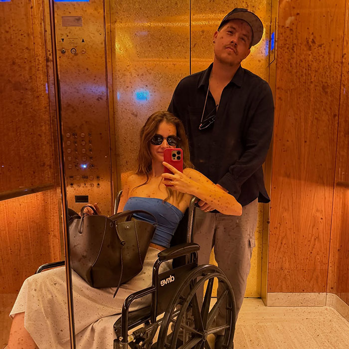 Woman in wheelchair taking selfie with man behind her in elevator, highlighting dark sides of Victoria&rsquo;s Secret models.