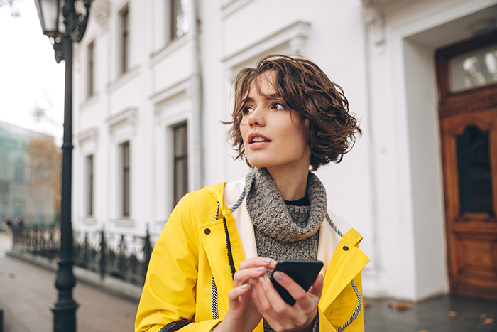 Young woman in a yellow jacket holding a phone outside, reflecting the story of rich folks firing babysitter with false accusations.