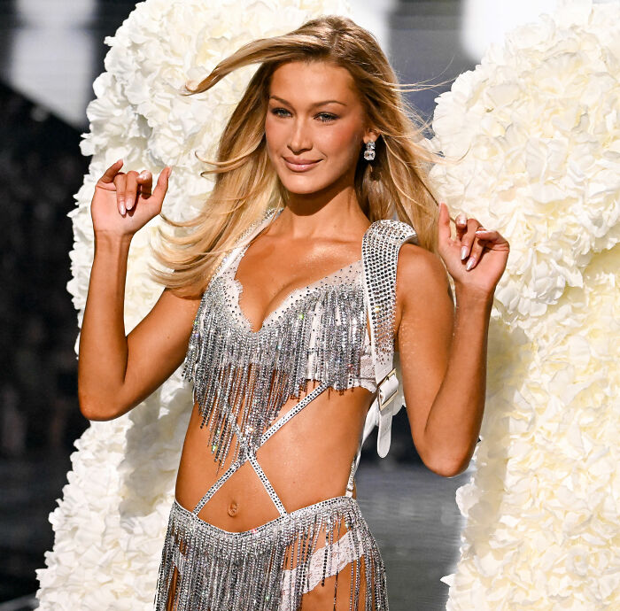 Victoria's Secret model walking runway wearing silver fringed lingerie and angel wings during fashion show.