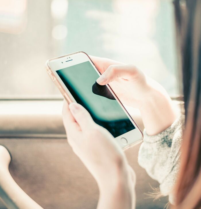 Woman holding smartphone inside car, symbolizing cheating signs in women shared by broken-hearted men.