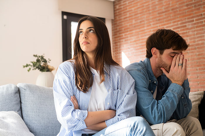 Couple sitting apart looking upset, illustrating guy fearing best man may go after his girlfriend after ex-wife's cheating.