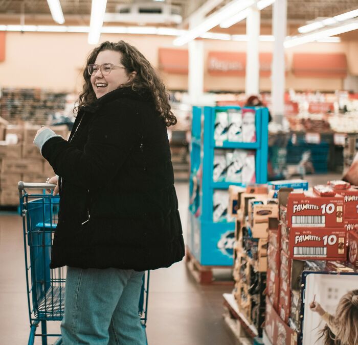 Pregnant woman smiling happily while shopping in a store aisle filled with various packaged goods on shelves.