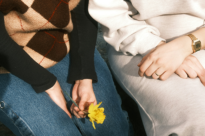 Two women sitting close, one holding a yellow flower, symbolizing the end of a friendship with 5 kids and 4 dads.