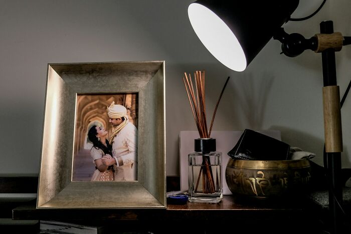 Photo frame with a couple on a table for two, next to a lamp and reed diffuser on a wooden surface.