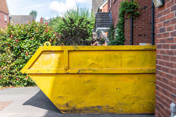 Yellow skip bin placed between brick houses, illustrating struggles of living next to horrible neighbors in residential area.