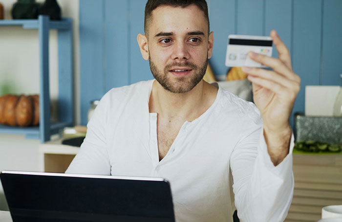 Young man using a laptop and holding a credit card while discovering loopholes in an online transaction at home.