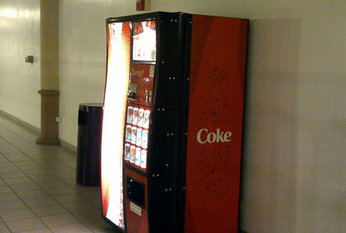 Coke vending machine in hallway with a hidden coin return, showcasing a clever loophole discovery.