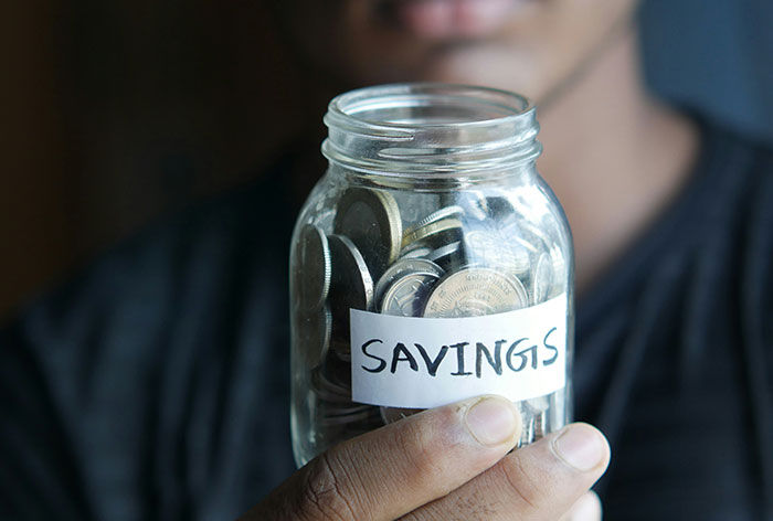 Person holding a jar labeled savings filled with coins, illustrating creative loopholes in saving money.