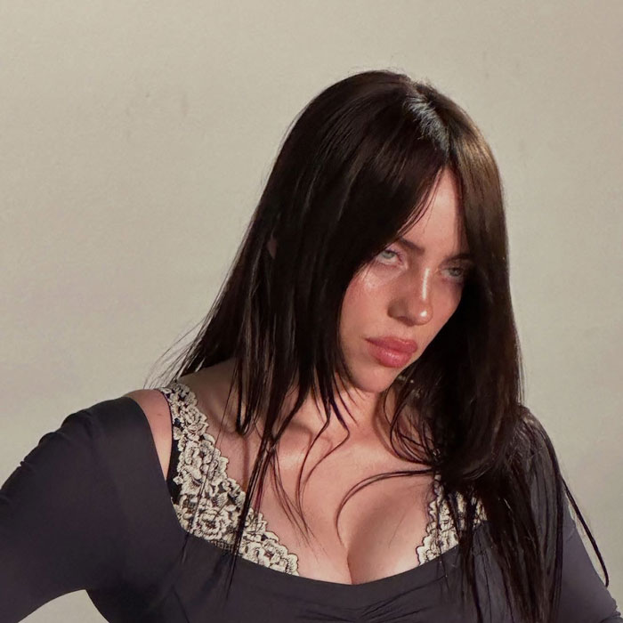 Billie Eilish with dark hair and lace top looking serious in a close-up photo related to Miami concert incident.