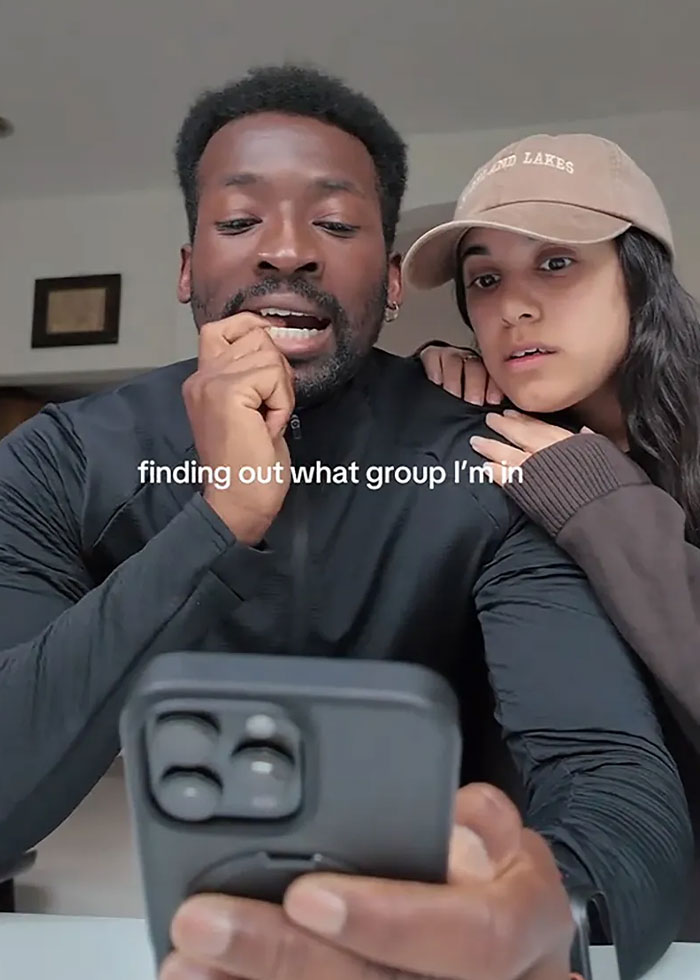 Two people looking at a phone with text about finding out what group they are in for viral Group 7 TikTok trend.