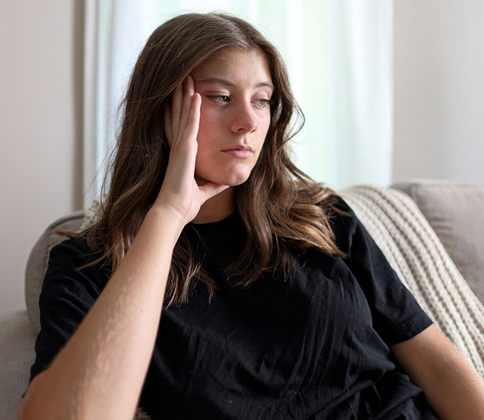 Young woman in a black shirt sitting on a couch, looking pensive and reflecting on toxic in-laws and newborn boundaries.
