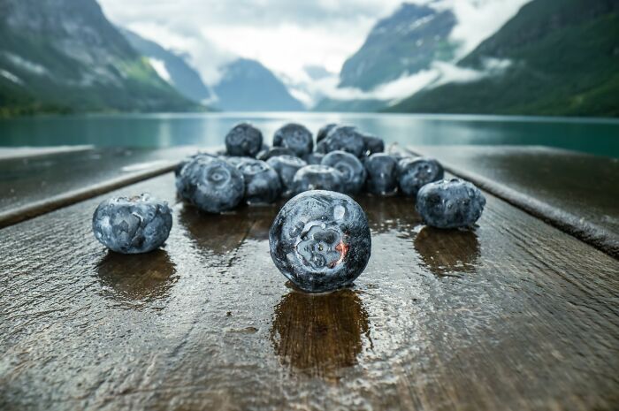Close-up of fresh blueberries on a wet wooden surface with mountains and lake in the background, highlighting unbelievable country facts.