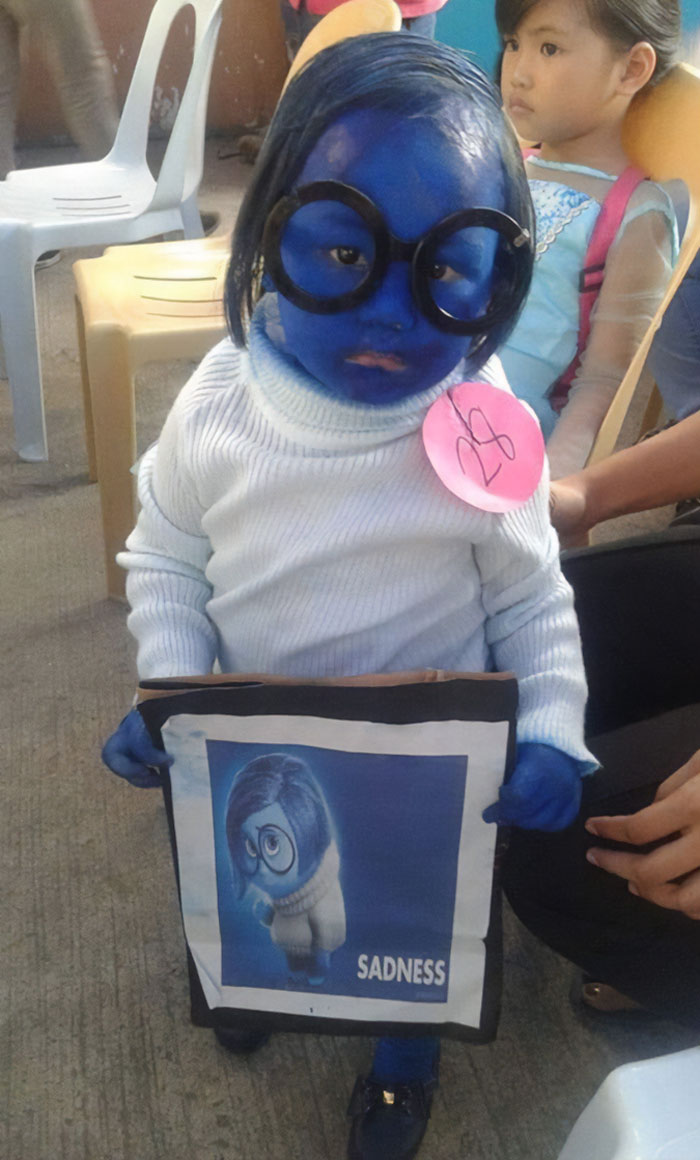 Child with blue face paint and glasses dressed as Sadness from Inside Out, a weird and funny picture from a costume event.