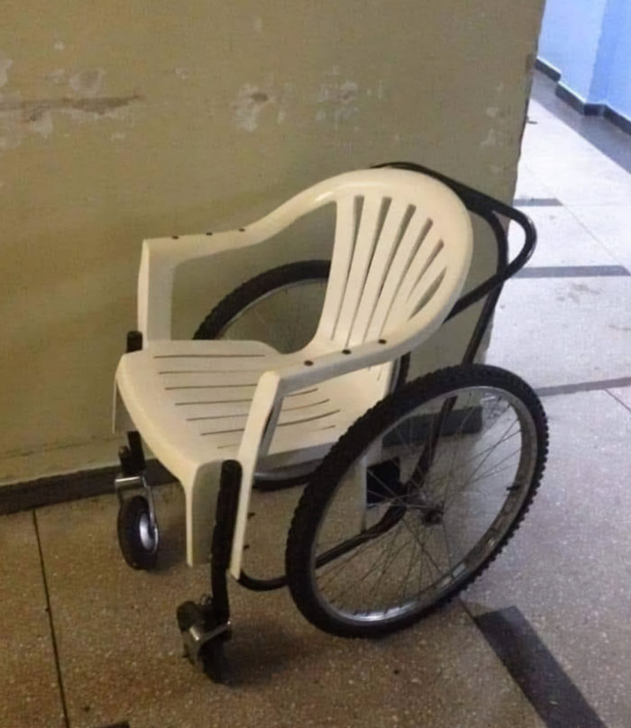 Plastic chair combined with wheelchair wheels creating a weird and cursed hybrid design in a dimly lit room.