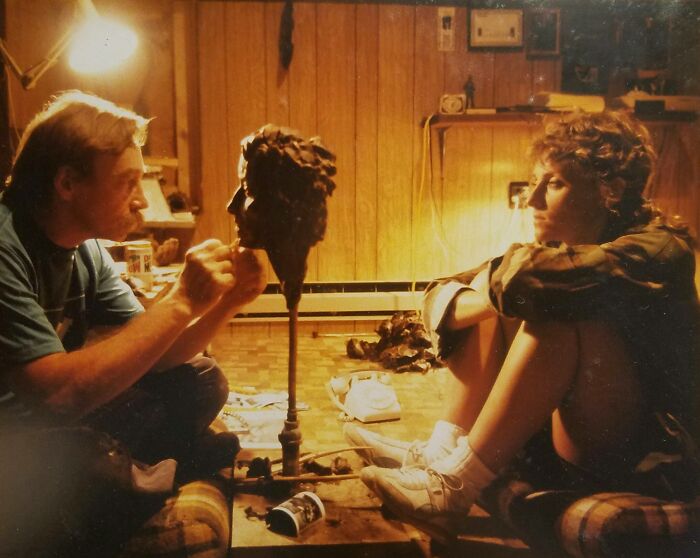 Man sculpting a head while a woman watches in a dimly lit room, capturing a wild and wonderful 1980s moment.
