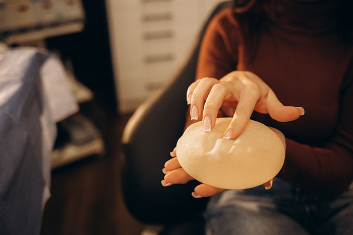 Woman holding a textured breast implant, illustrating botched plastic surgeries and their unfortunate outcomes.