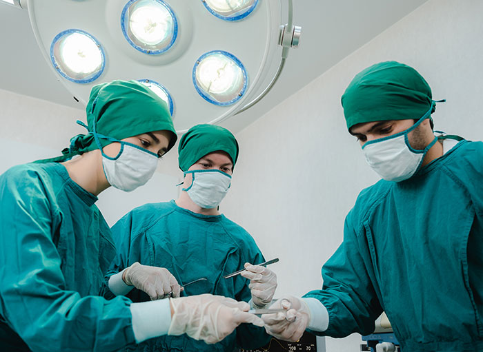 Surgeons in green scrubs and masks performing a procedure under bright operating room lights focused on plastic surgeries.