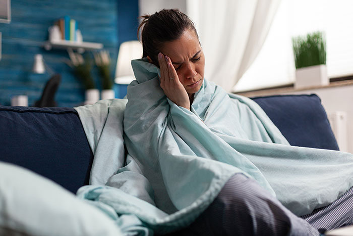 Woman wrapped in a blanket sitting on a couch holding her face in pain, illustrating botched plastic surgeries experience.