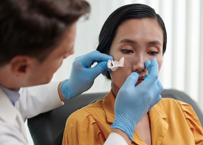 Doctor wearing blue gloves examining a woman’s face, addressing botched plastic surgery concerns in a clinical setting.