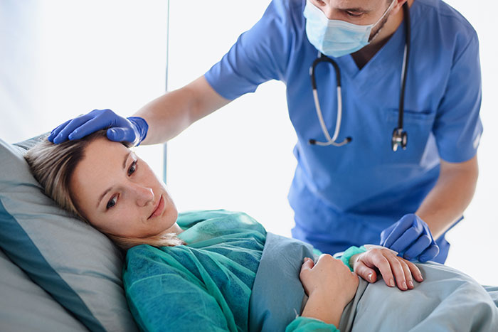 Doctor in mask comforting a woman in hospital bed, illustrating the worst stories of botched plastic surgeries experienced.