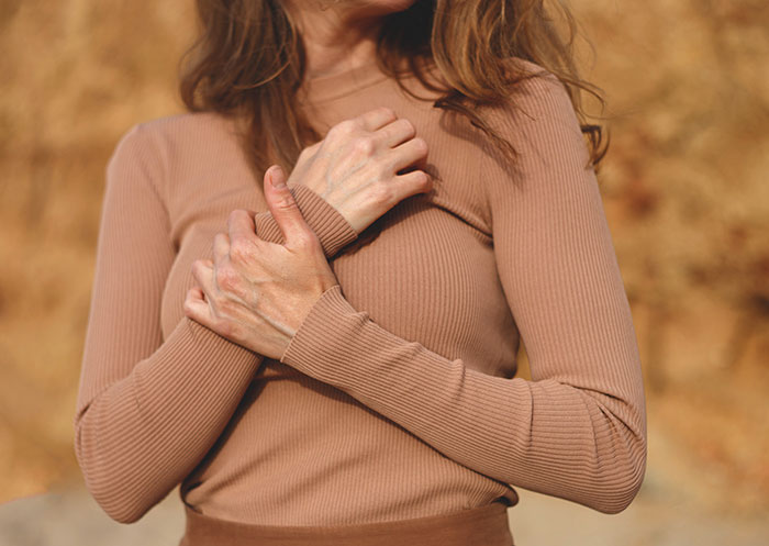 Woman in brown shirt holding her chest, conveying pain and discomfort related to botched plastic surgeries experiences.