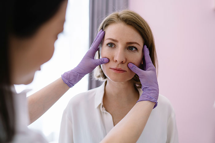 Medical professional examining a woman's face, highlighting issues related to botched plastic surgeries experienced by patients.