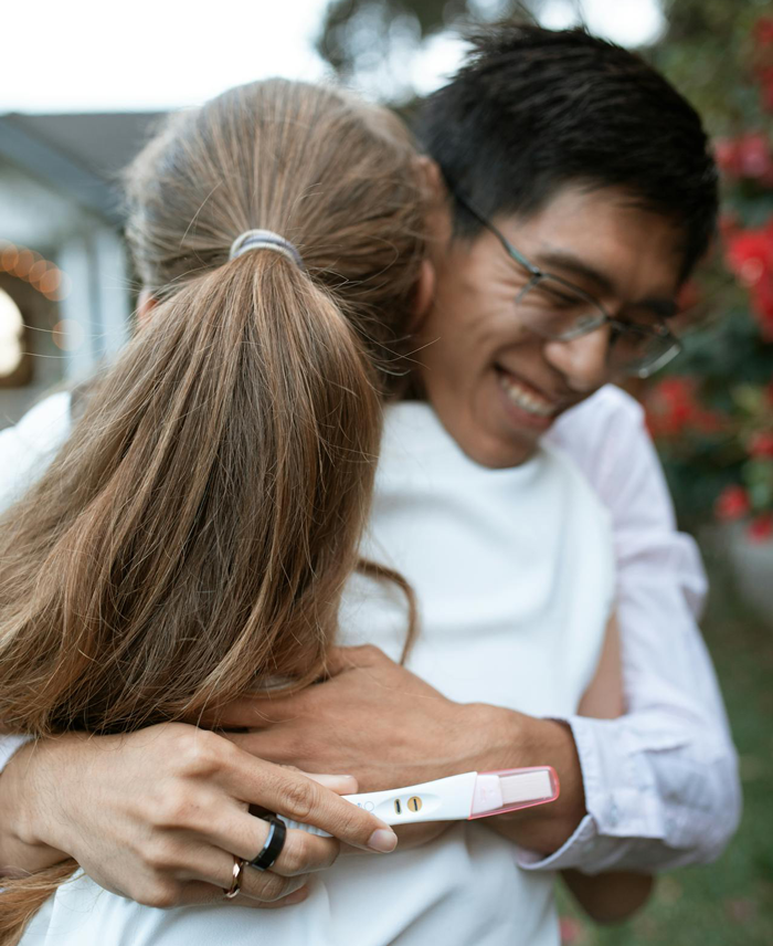 Couple hugging outdoors with a positive pregnancy test, highlighting pregnant girlfriend feeling too sore and tired.