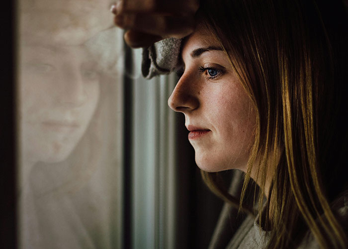 Young woman looking thoughtfully out a window, reflecting on a man with debt asking for a loan to buy a Spiderman costume.