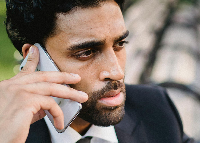 Close-up of a man with $5K debt making a serious phone call, possibly discussing a loan for a Spiderman costume purchase.