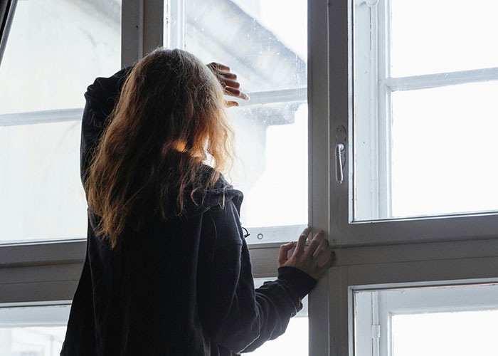 Woman looking out a window in contemplation, symbolizing the dilemma of a man with debt and a costly Spiderman costume loan request.