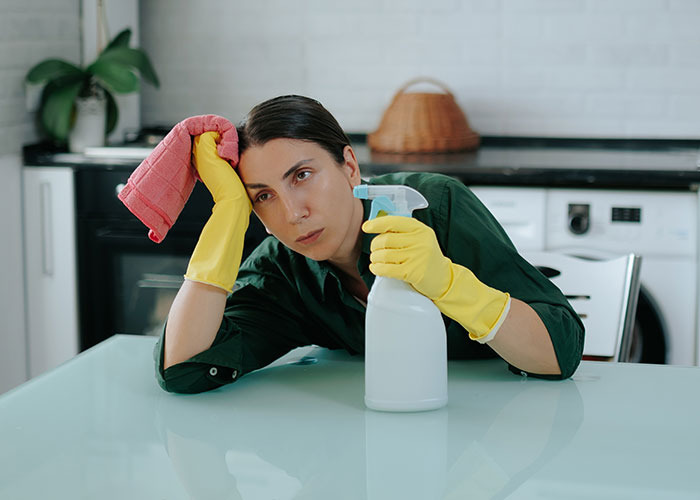 Woman called a gold digger wearing yellow gloves, holding cleaning spray and cloth, looking frustrated in kitchen.