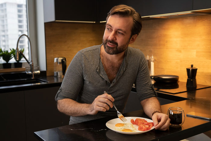 Man eating breakfast alone in kitchen, reflecting on boyfriend mother family expectations and relationships.
