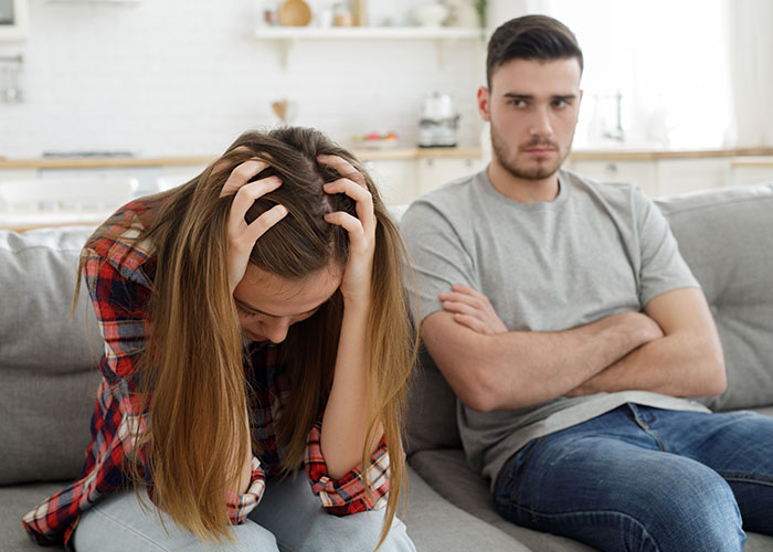 Upset girlfriend and man in gray shirt sitting apart on couch over work wife sending hearts and mirror selfies. Upset girlfriend and man in gray shirt sitting apart on couch over work wife sending hearts and mirror selfies.