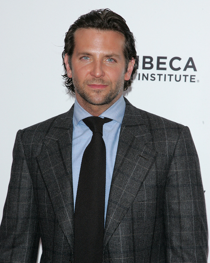 Bradley Cooper attending an event in a gray plaid suit and black tie, showcasing his radical makeover look.