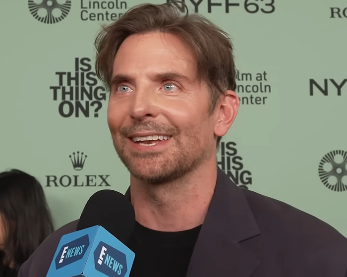 Bradley Cooper with a radical makeover at a premiere, smiling and speaking into an E News microphone.