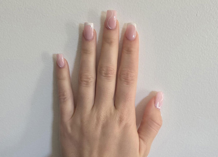 Close-up of a bridesmaid&rsquo;s hand with freshly done light pink nails before a wedding, showing polished acrylic nails.