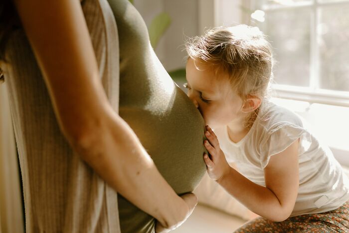 Young child kissing a pregnant belly in a sunlit room, illustrating common truths people were fooled into believing.
