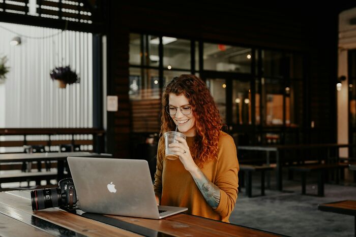 Young woman with glasses using laptop and drinking coffee in a café, representing people who lost jobs to AI experiences.