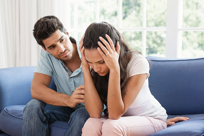 Man comforting upset woman on couch after Thanksgiving argument causing shock and horror in family gathering.