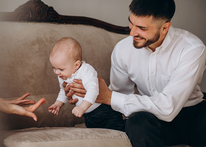 Man holding baby on couch, smiling and interacting, illustrating family dynamics with multiple children and women.