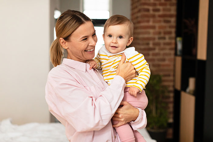 Woman holding baby smiling indoors, illustrating a live-in nanny job with challenging demands story context.