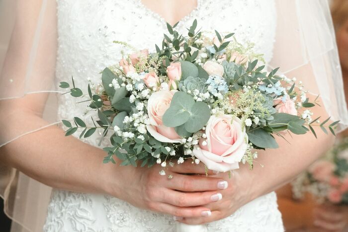 Bride holding a bouquet of pink roses and greenery, illustrating wedding guests making the bride and groom regret knowing them.