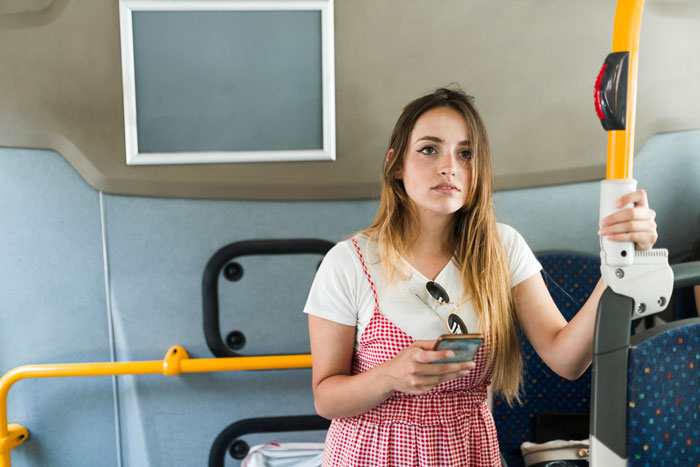 Teen woman standing on bus holding a pole and smartphone, illustrating conflict involving disabled man on public transport. Teen woman standing on bus holding a pole and smartphone, illustrating conflict involving disabled man on public transport.