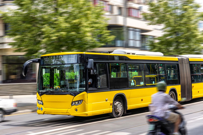 Yellow city bus driving through a street with blurred traffic in the background in urban environment. Yellow city bus driving through a street with blurred traffic in the background in urban environment.