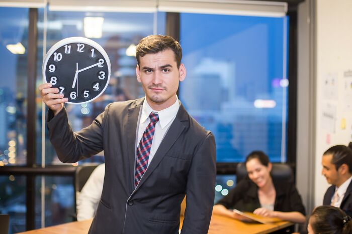Man in business suit holding clock in office, illustrating positive stereotypes people have about various countries.