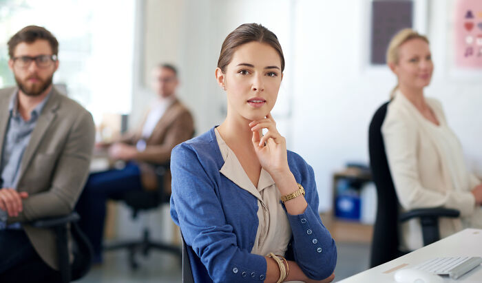 Young accountant in a blue blazer thoughtfully posing in an office with colleagues, illustrating accountants and their surprising stories.