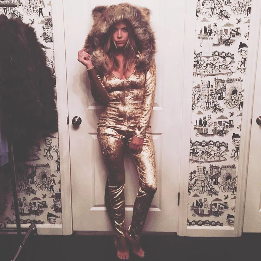 Celebrity posing in a shiny gold Halloween costume with a large furry hood, showing lack of common sense in outfit choice.