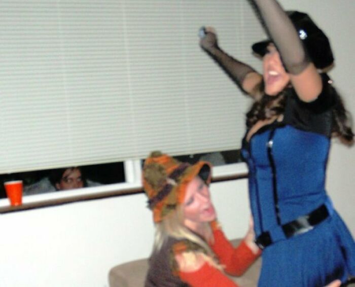 Person peeking creepily through window blinds while two women dance inside, capturing a creepy photo moment.