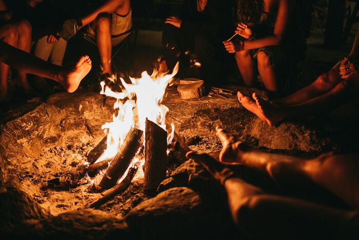 Group of people relaxing barefoot around campfire at night, illustrating times the universe protected them from harm.